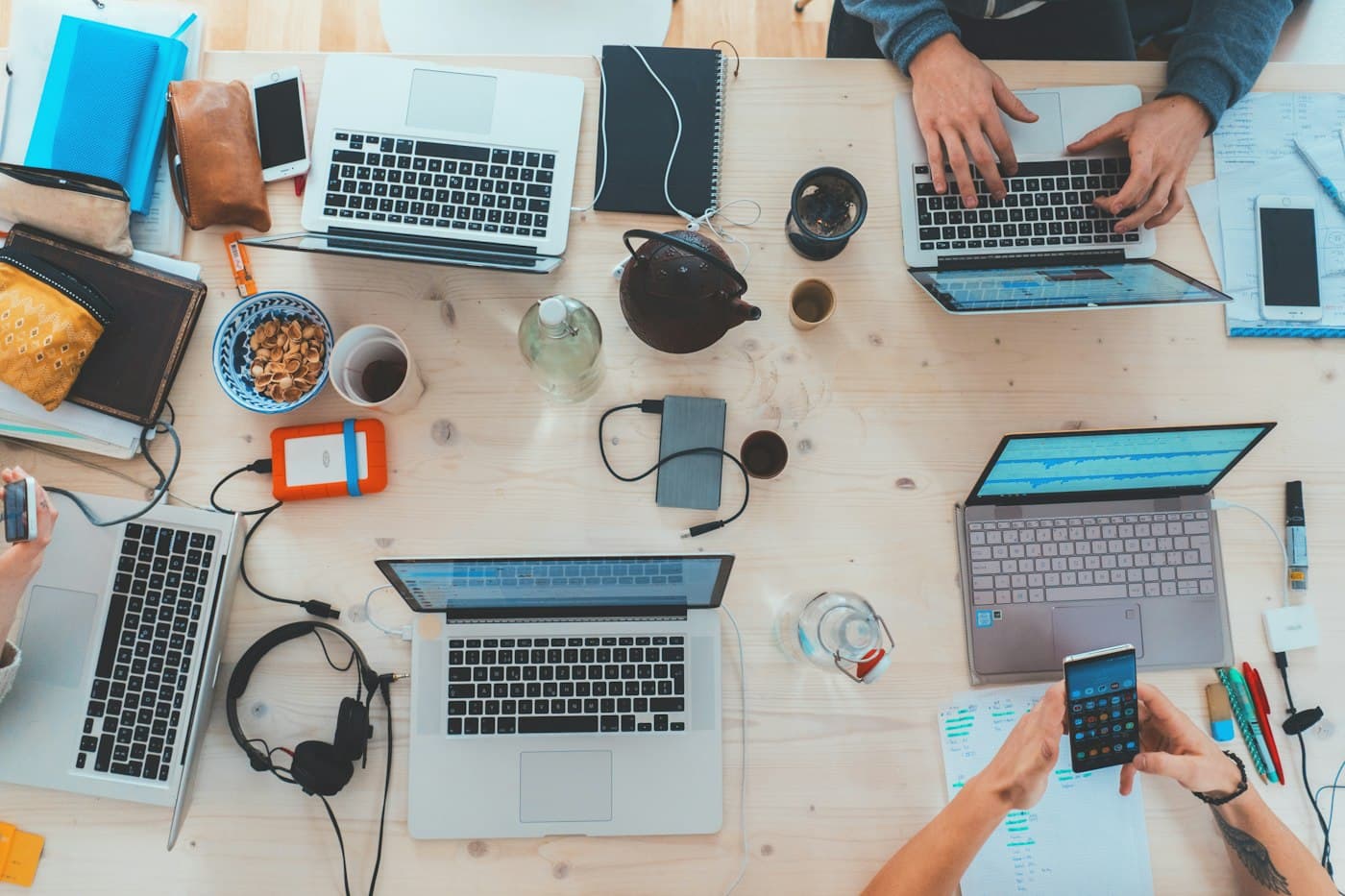 Overhead view of a shared desk covered in laptops, notebooks and phones