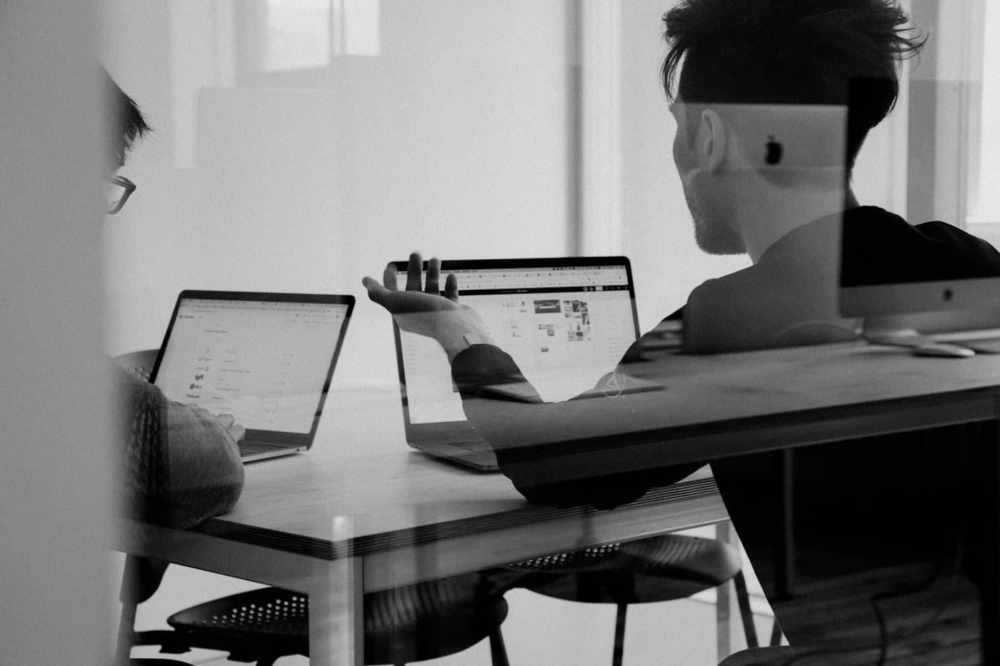 Two colleagues discussing a website on laptops, seen through glass