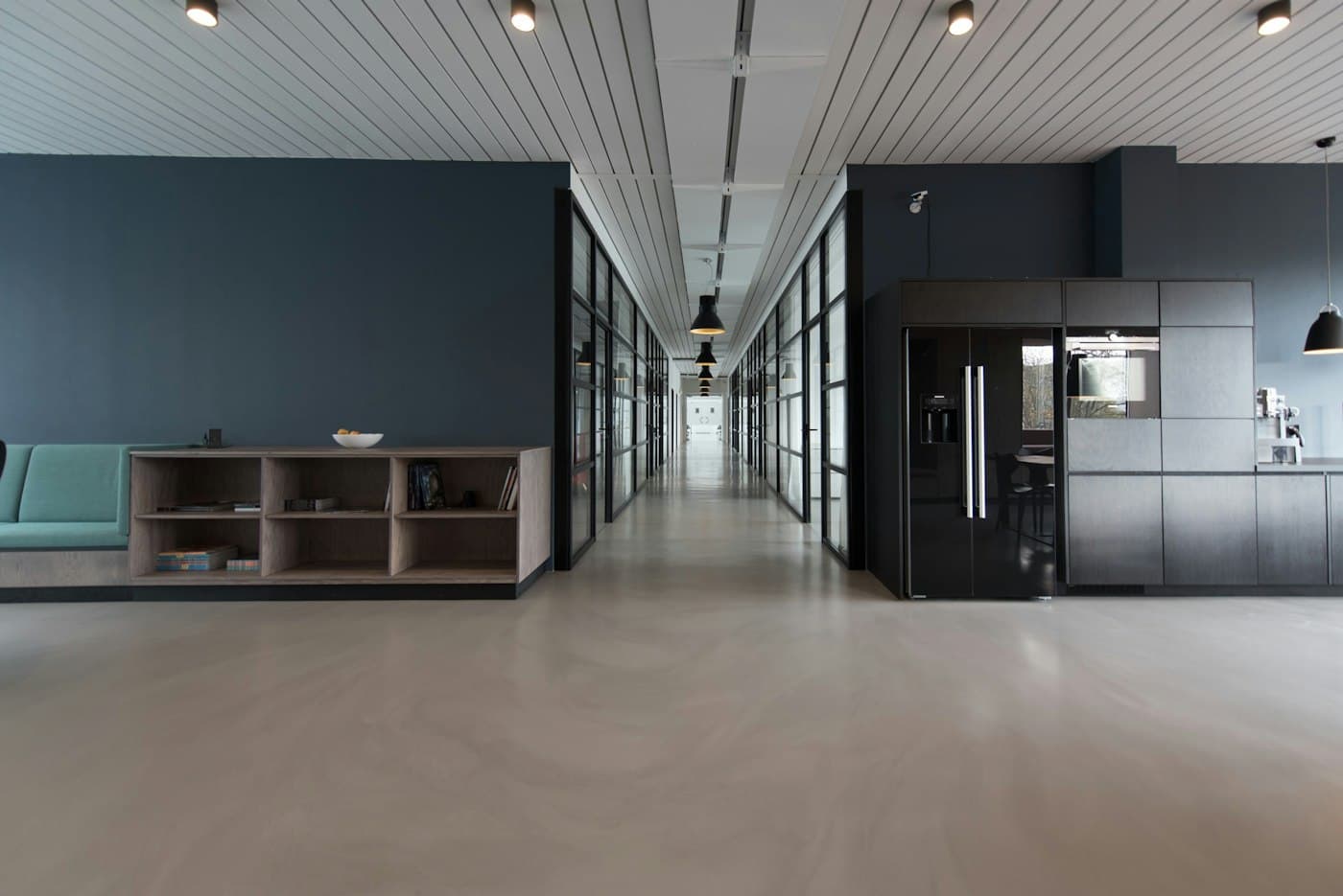 Long glass-walled office corridor with a kitchen and lounge