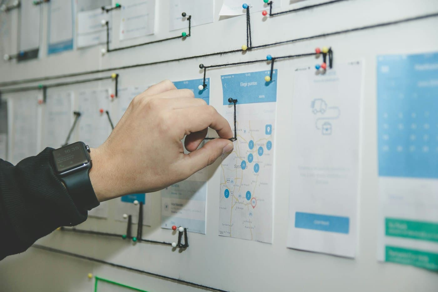 A hand pinning a user-flow map onto a wall of app screens