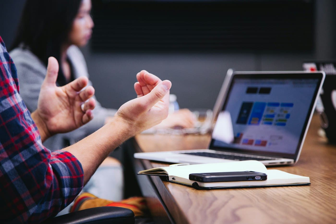Hands gesturing in a meeting beside a laptop showing a design board